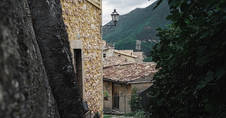 Alleyway in Poggiodomo with stone houses, terracotta roofs, and a view of the green Umbrian mountains.