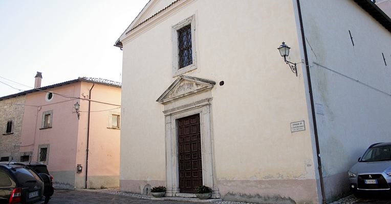 Façade of the Church of Saint Charles Borromeo in Poggiodomo, featuring a Renaissance portal and a grated window.