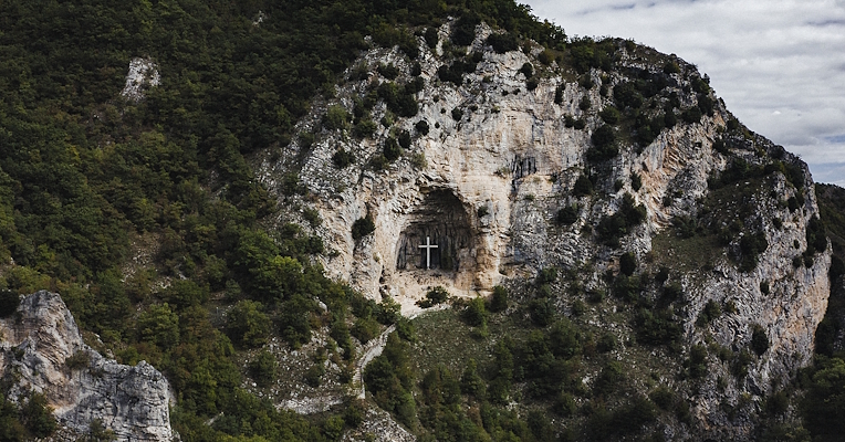 View of the Grotta d’Oro of Roccaporena, a spiritual refuge carved into the rock with a cross, surrounded by Cascia’s woods.