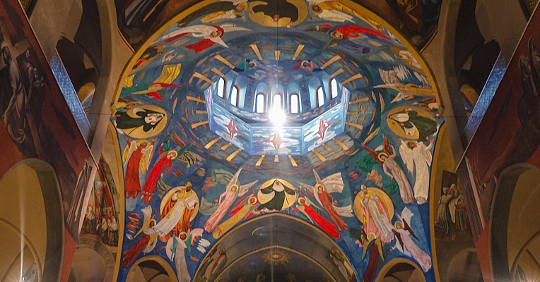 Frescoed vault of the Basilica of Saint Rita of Cascia, with colourful angels and light filtering through the dome’s lantern.