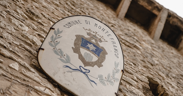Sign with the coat of arms of Montefranco on a stone wall, seen from below with a perspective angle.