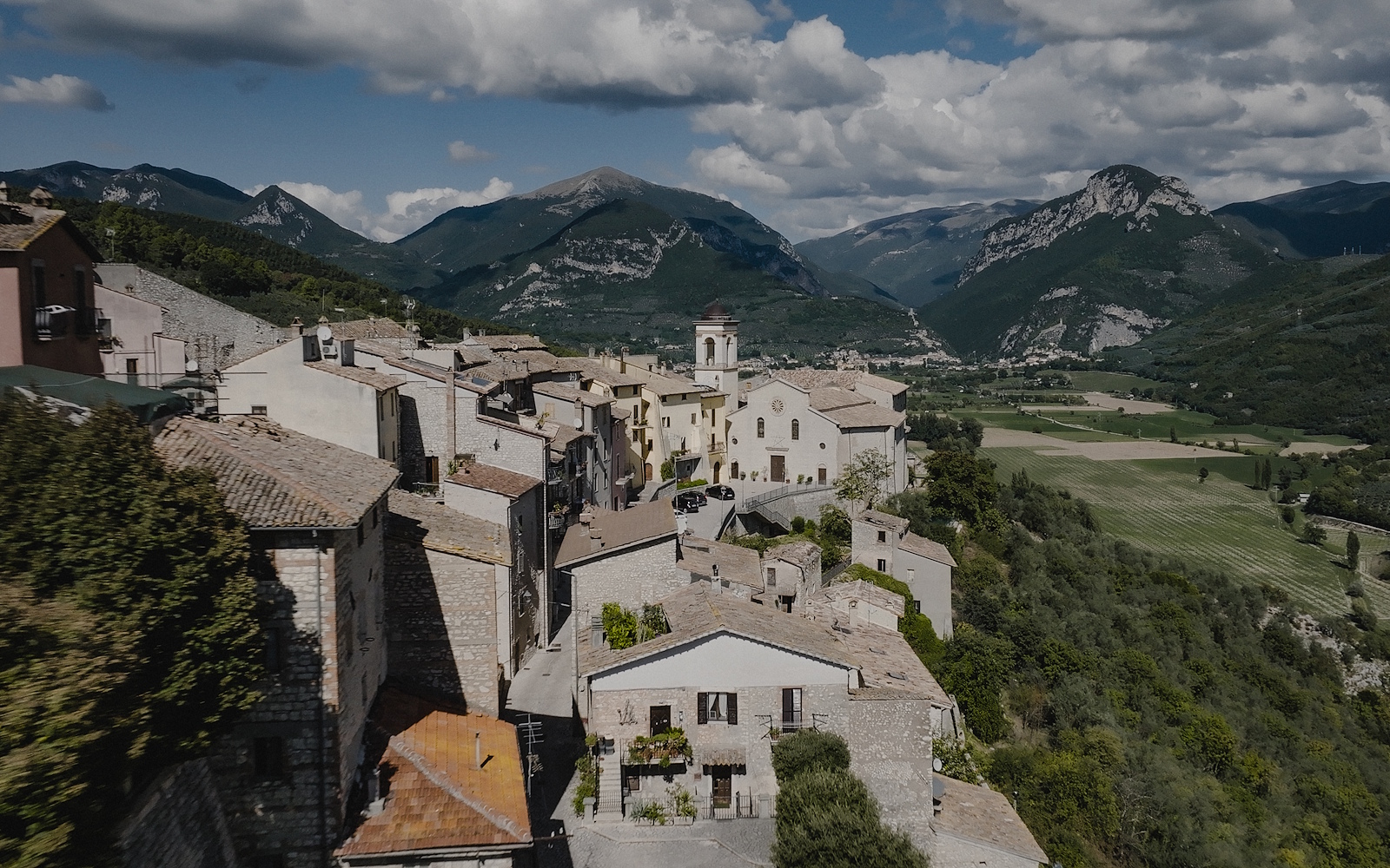 Aerial view of Montefranco, a perched Umbrian village with central church, stone roofs and green mountains in the background.
