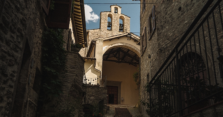 Stone staircase between stone houses in Scheggino leading to the sunlit Church of San Nicola.