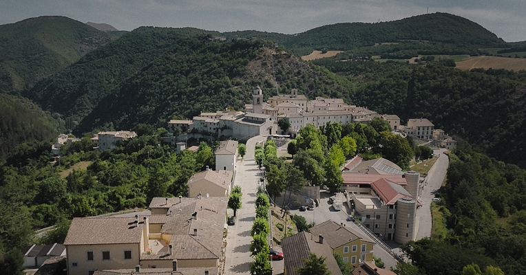 Aerial view of Sellano, an Umbrian village surrounded by green hills and woods, with stone houses and terracotta roofs.
