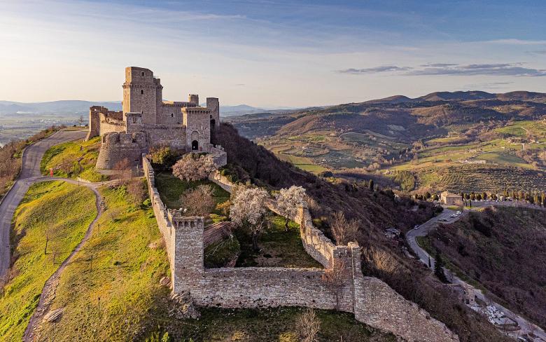 Immagine: Aerial view of the Rocca Maggiore in Assisi, surrounded by medieval walls, overlooking the valley amid Umbrian hills. 