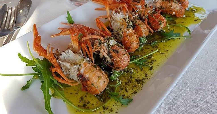 Gamberi serviti su un letto di rucola con salsa verde, impiattati su un vassoio bianco in ristorante elegante. (Photo credits: TRATTORIA TERESA)