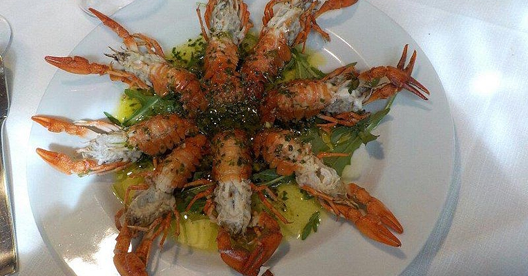 Prawns arranged in a sunburst on a white plate, with green sauce and rocket.