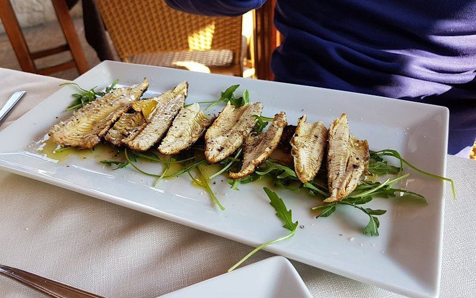 Grilled lake fish fillets (carbonaretti), served on a bed of rocket with extra virgin olive oil, plated on a white dish. (Photo credits: TRATTORIA TERESA)