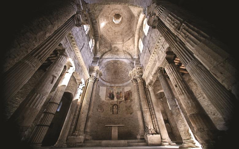 Immagine: Intérieur de la basilique de San Salvatore à Spolète, avec colonnes antiques, abside ornée de fresques et coupole voûtée. 