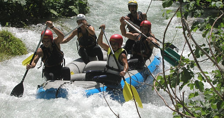 Rafting boat with five people on board paddling in the current of a river.