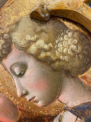 Detail of a Renaissance painting with the face of an angel with blond curls and golden halo.