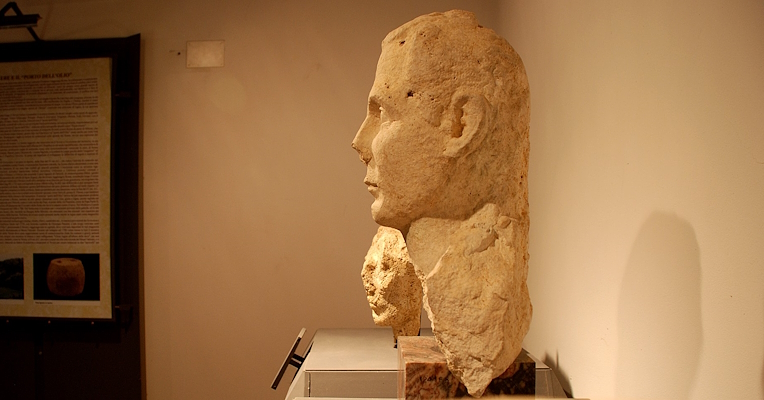  Side view of a stone Roman bust on display on a pedestal. 