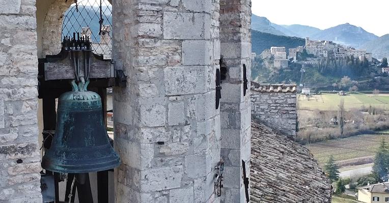 Campana di bronzo in una torre campanaria in pietra, con un castello medievale sullo sfondo