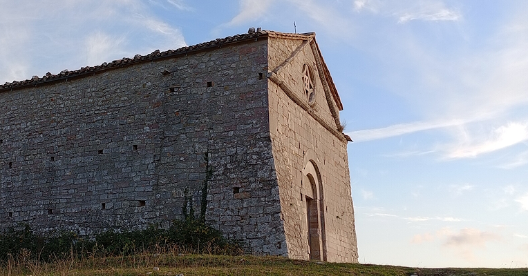 Side view of a stone building located on a grassy hill, with a blue sky and light clouds in the background.