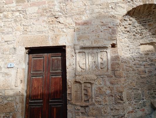 Dark wooden door set in a stone wall with reused materials and carved Roman reliefs.