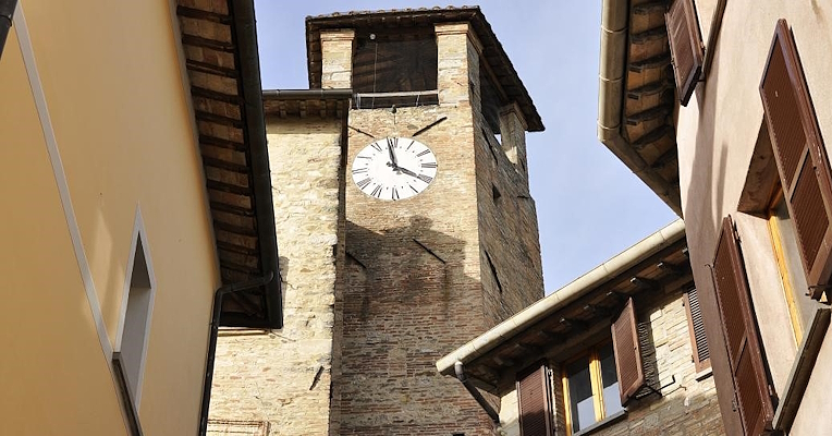 Civic tower with clock in Montone, framed by the roofs and façades of the village houses.