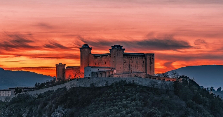 Die Albornoz-Festung, die bei Sonnenuntergang über der Stadt Spoleto thront, beleuchtet von einem feurig roten Himmel