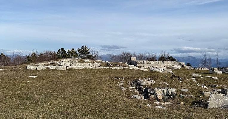 Ruines en pierre sur une colline herbeuse avec vue panoramique sur les collines et les montagnes à l’horizon sous un ciel nuageux.