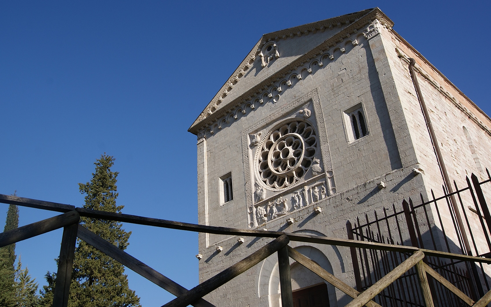 Romanesque façade of the Abbey of Saints Felix and Maurus in Castel San Felice, with carved rose window and clear sky.