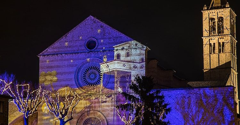 Christmas light projections on the façade of the Basilica of Assisi with illuminated trees.