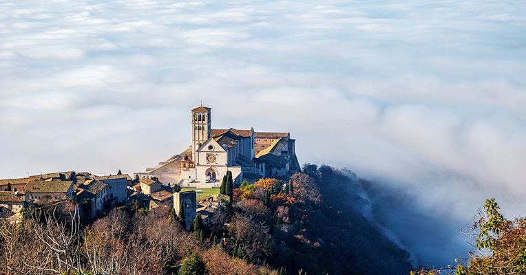 The Umbrian Valley wrapped in winter fog, with the Basilica of Saint Francis of Assisi standing out under the sunlight.