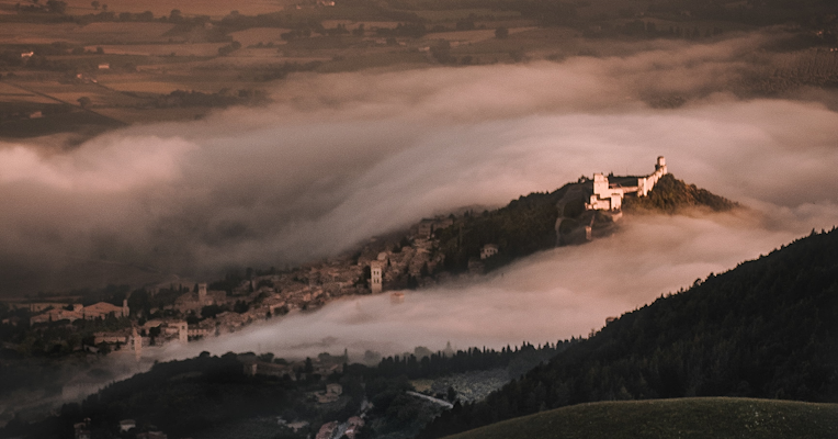 The Umbrian Valley wrapped in winter fog, with the Basilica of Saint Francis of Assisi standing out under the sunlight.