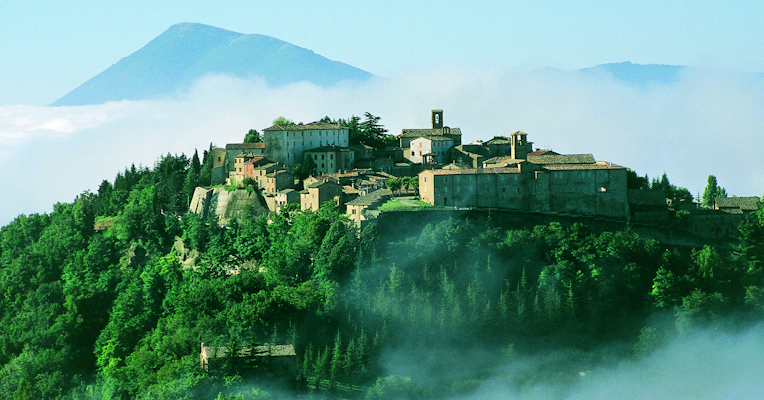 The village of Montone under a sunlit sky, with the Upper Umbrian Valley in the background, wrapped in winter mist.