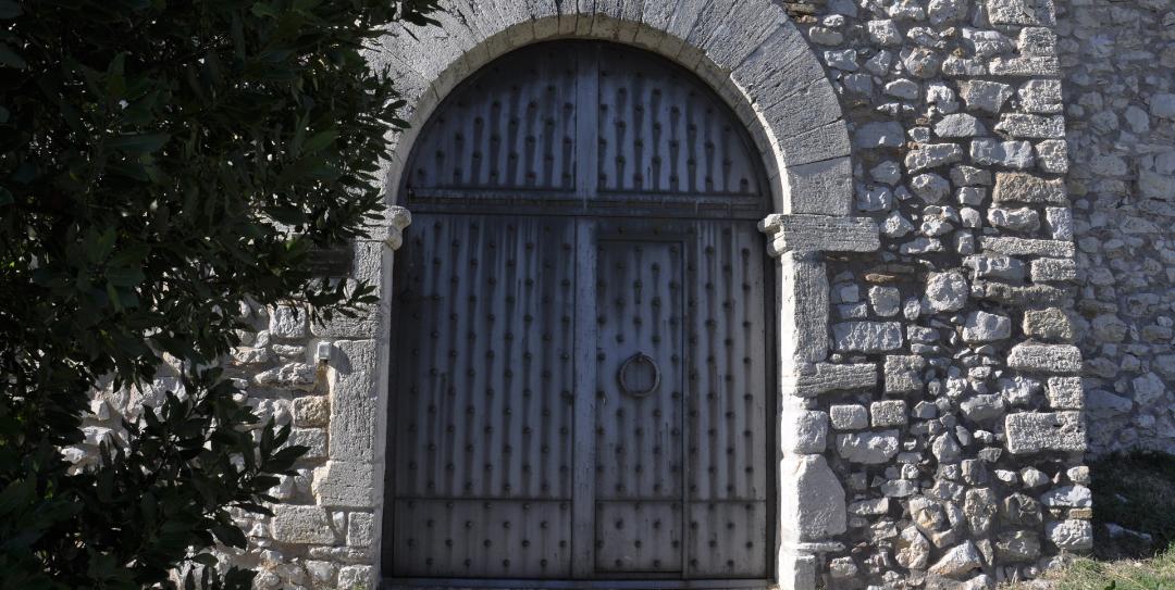 Porte en bois renforcée de clous en fer, encadrée par une arche en pierre sur les murs du Castello del Poggio.