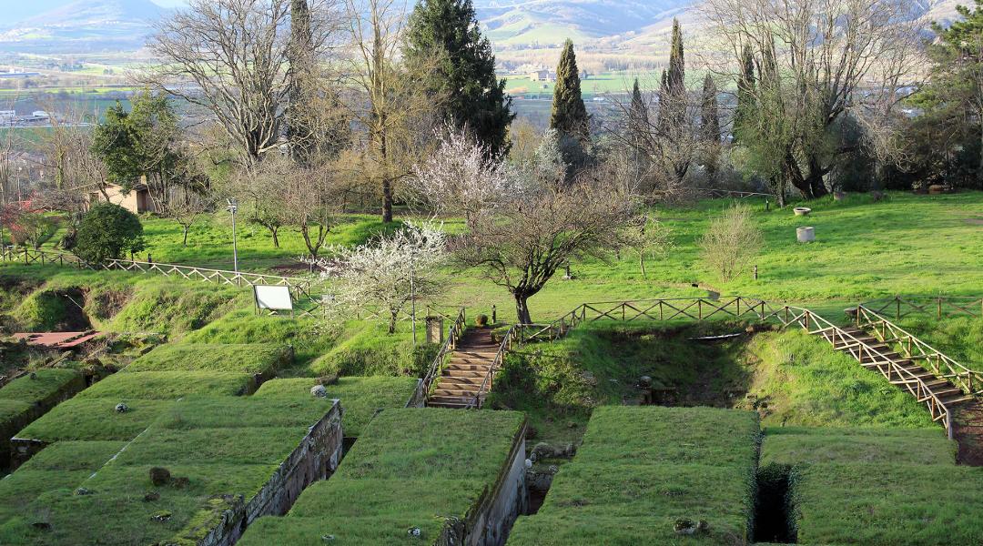 Vue aérienne de la nécropole étrusque avec tombes à tumulus recouvertes d’un toit herbeux, entourée de collines.