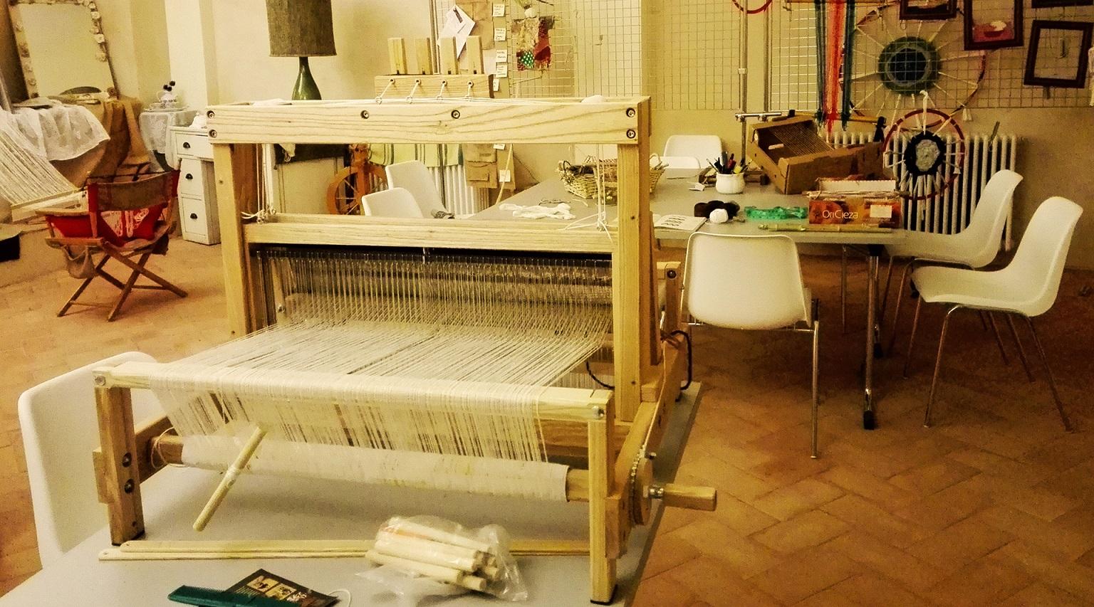 In the foreground, an ancient weaving loom is clearly visible, while in the background there is a table equipped for other types of artisanal work.