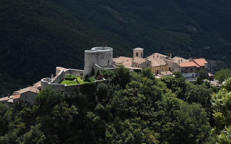 Veduta aerea di Polino, borgo medievale umbro con una torre circolare e mura fortificate, immerso tra boschi verdi.
