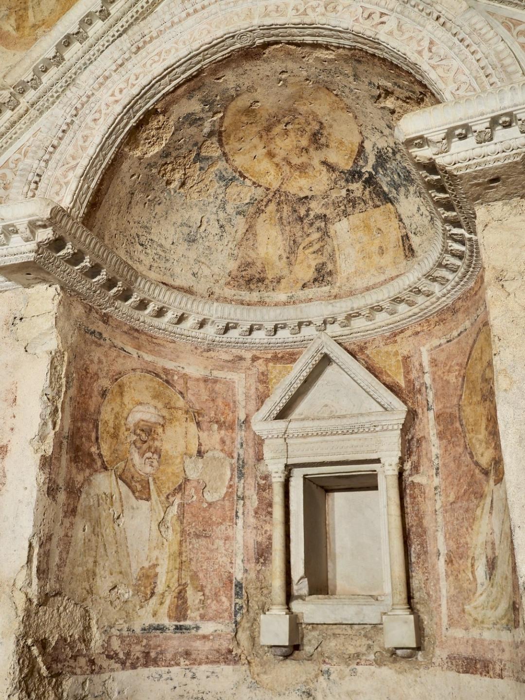 Detail of the ancient interior frescoes of the Tempietto del Clitunno, featuring a stone niche and frescoes depicting saints