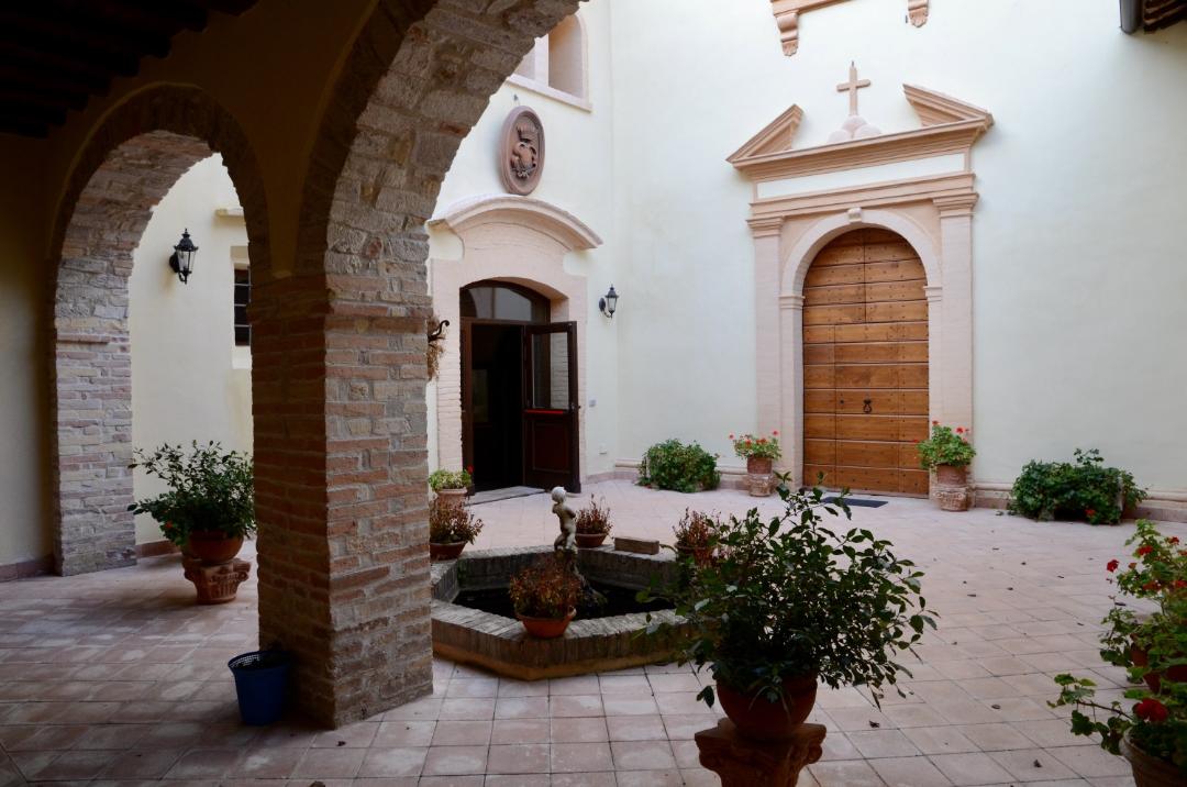 Cloître avec arches en pierre, cour centrale avec fontaine et plantes en pot