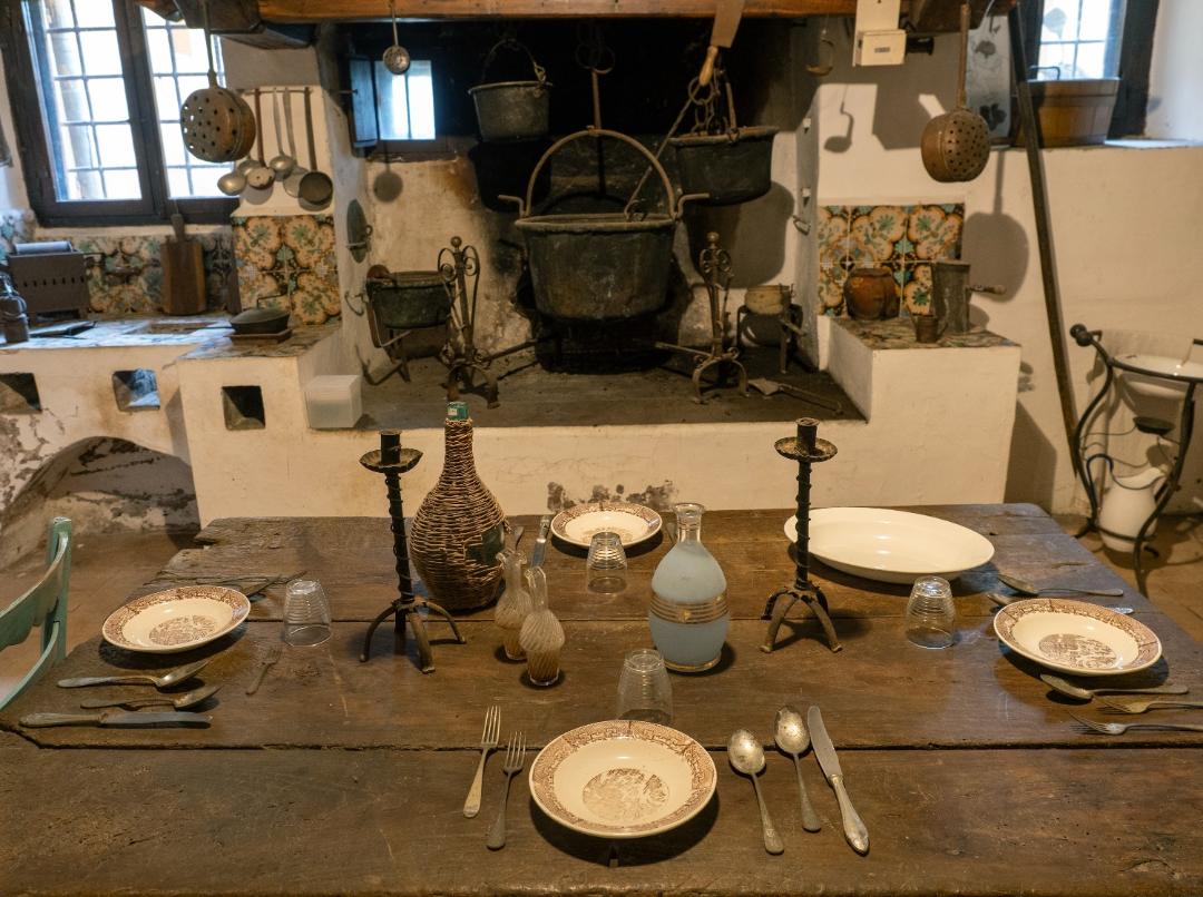 Wooden table with plates, cutlery, bottles and candlesticks in front of the large hearth with hanging pots