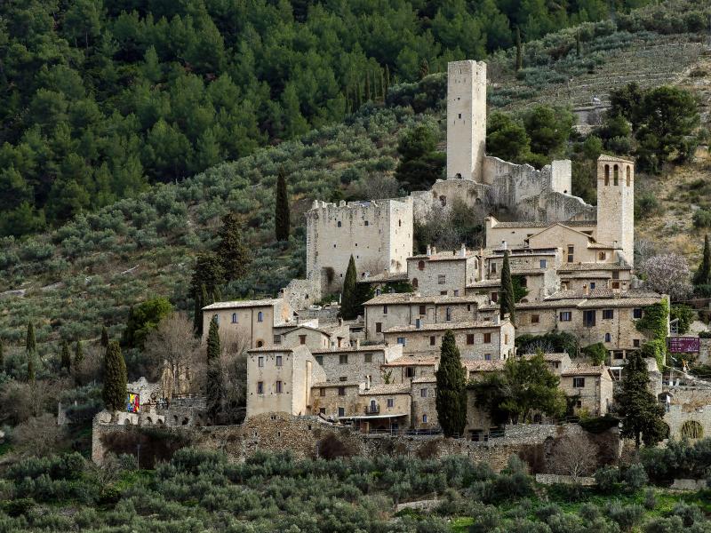 Burg Pissignano Alto, mit mittelalterlichen Türmen und Steinhäusern, eingebettet zwischen Olivenhainen und bewaldeten Hügeln