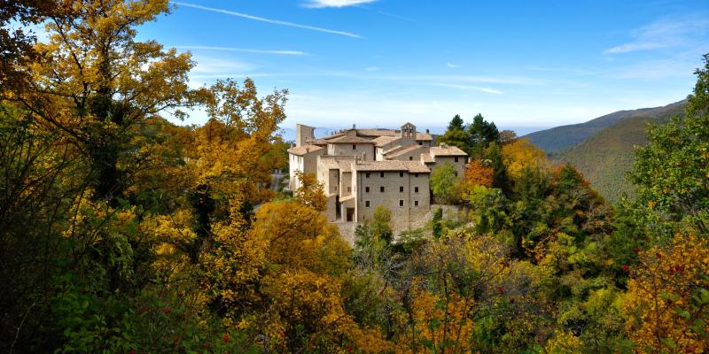 Castello di Acera immerso tra i boschi autunnali dell’Umbria, con foglie gialle e arancioni che incorniciano le case