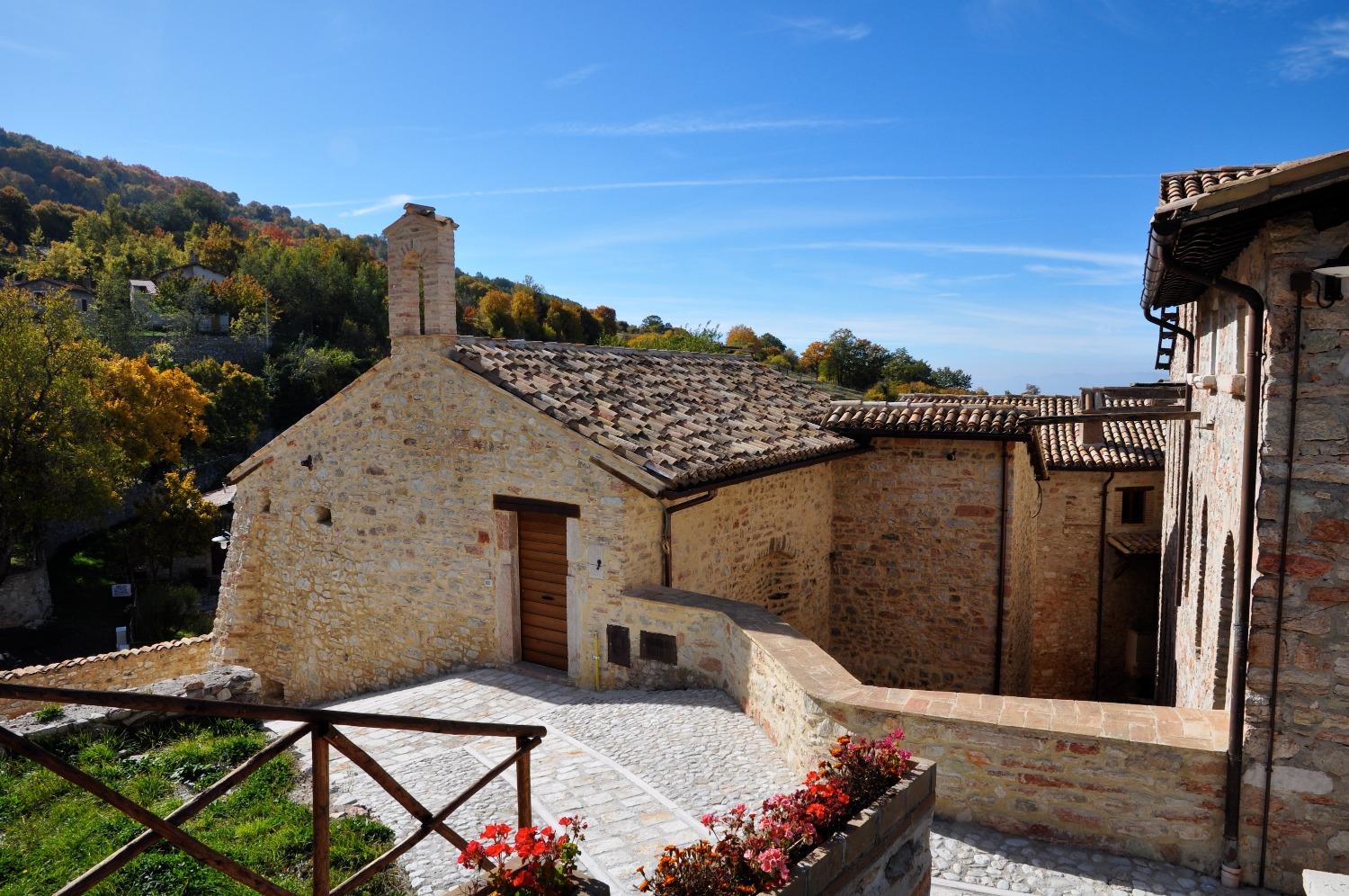 Stone houses of Acera with old roofs and a flowered terrace overlooking the woods