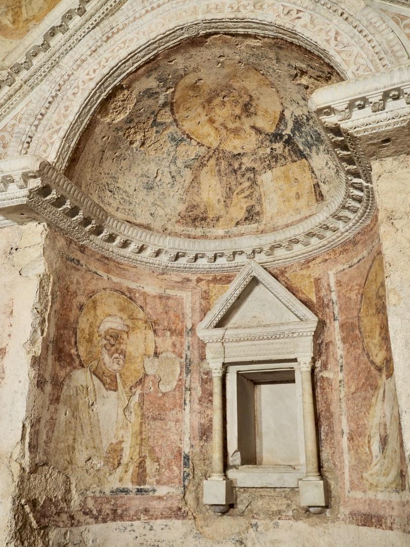 Detail of the ancient interior frescoes of the Tempietto del Clitunno, featuring a stone niche and frescoes depicting saints