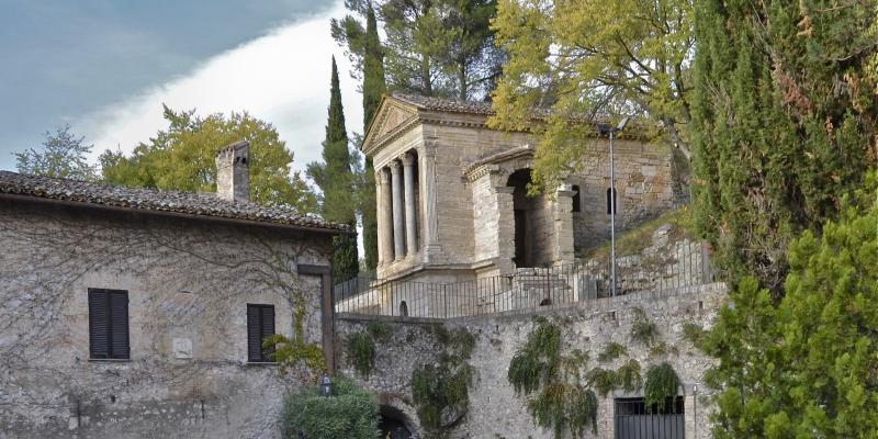 Das Tempietto del Clitunno, ein langobardisches, tempelartiges Bauwerk mit Säulen und Giebel, eingebettet im Grün der umbrischen Landschaft