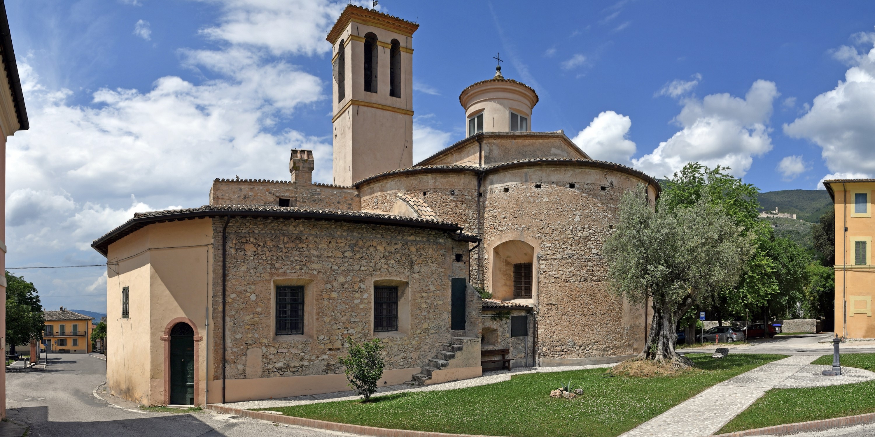 Church of Madonna della Bianca seen from the back, with its bell tower and rounded apse, set within the village of La Bianca