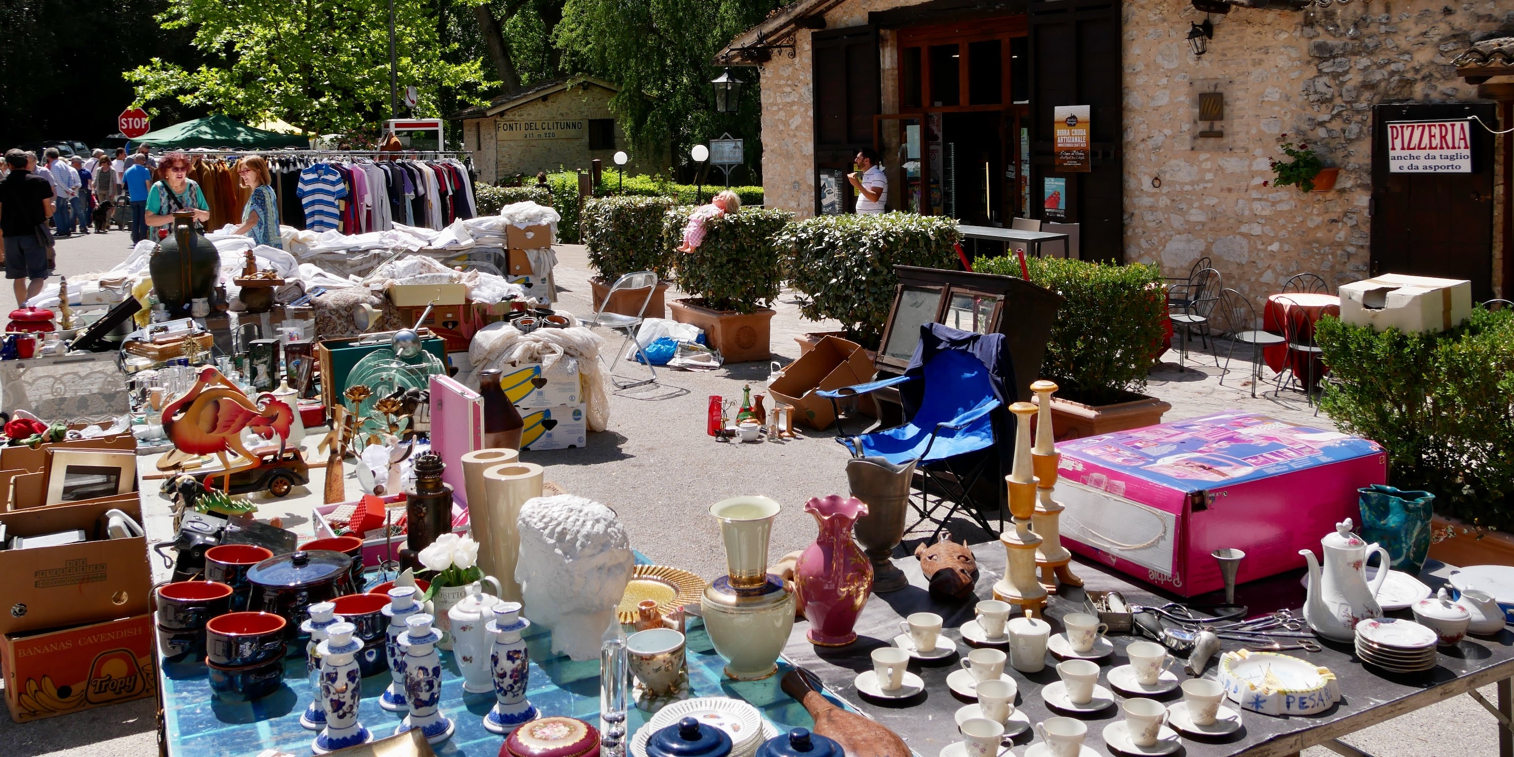 Stalls of an antique market with ceramics, vintage items and clothes displayed outdoors near the Fonti del Clitunno
