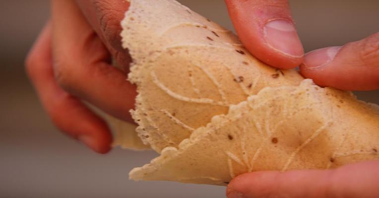 Mani che reggono un cono realizzato con una cialda artigianale, con disegni impressi e semi di anice