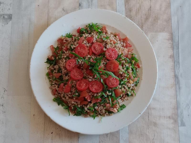 Piatto di insalata di farro con pomodorini tagliati e rucola fresca servito su tavolo in legno chiaro, vista dall’alto