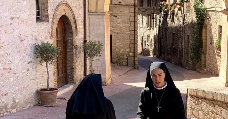 Elena Sofia Ricci, nei panni di Suor Angela, con un'altra suora in un vicolo medievale soleggiato di Assisi.